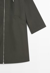 Dark green coat with three-quarter sleeve, diagonal slit pocket, and front silver zipper on white background.