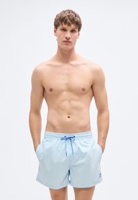 Ανοιχτό μπλε μαγιό σορτς από λείο ύφασμα με ελαστική μέση και κορδόνι. Διαθέτει μικρό λογότυπο στην αριστερή πλευρά.