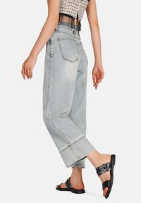 Jeans in denim azzurro chiaro a vita alta con gambali larghi e orlo sfrangiato, abbinati a sandali neri piatti con una cinghia decorata.