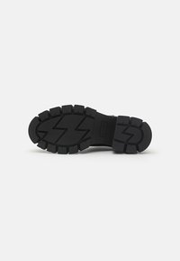 Rubber footwear sole in black, featuring a rugged tread pattern with zigzag details. Thick, textured construction for durability and grip.