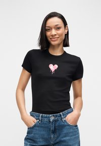 Camiseta negra ajustada con un gráfico de corazón rosa con efecto de goteo en el centro. Hecha de tela suave, con mangas cortas y escote redondo.