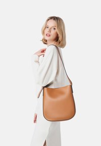 Borsa a spalla in pelle beige con una texture liscia e curve morbide, caratterizzata da una tracolla scura in contrasto e un design minimalista.