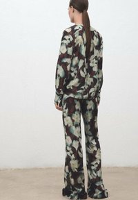 Conjunto de loungewear con estampado floral que incluye una blusa de corte suelto y pantalones de pierna ancha. La tela combina tonos marrón oscuro, crema y verde con una textura suave.