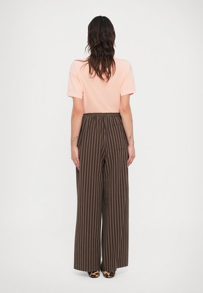 Απαλό ροζ t-shirt, σε άνετη εφαρμογή, σε συνδυασμό με καφέ ριγέ παντελόνες με φαρδιά πόδια που έχουν κάθετες γραμμές και ελαστική μέση.