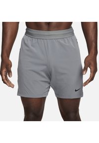 Pantalones cortos deportivos grises con cintura elástica y bolsillos laterales. Presenta un logo negro de Nike en la pierna izquierda con una tela liviana.