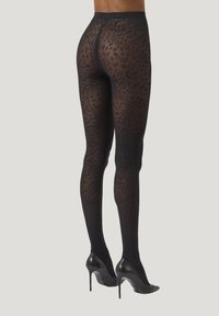 Svarta djurmönstrade leggings i genomskinligt material, med ett mönsterskapat design, elastiskt midjeband, och bärs med svarta högklackade skor.