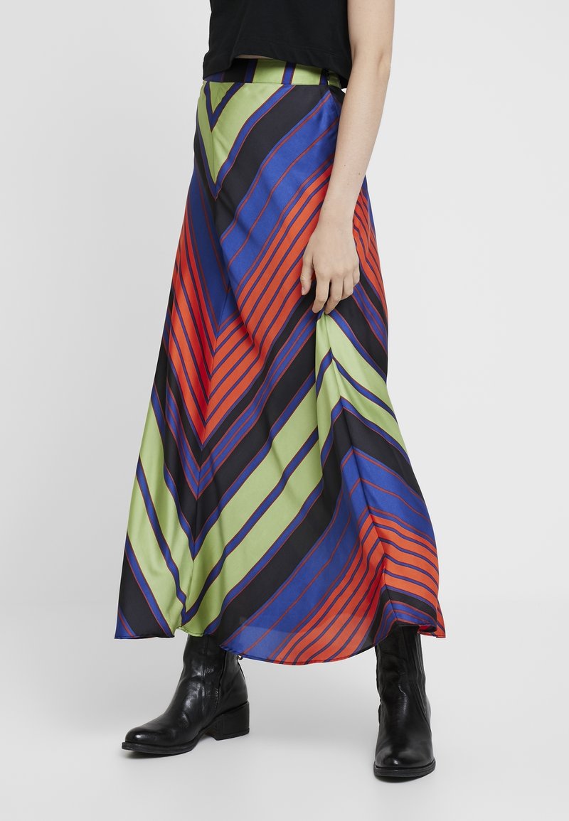 Jupe maxi en tissu léger avec des rayures diagonales vibrantes en rouge, bleu, vert et noir. Elle possède une taille haute et une silhouette fluide.