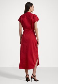 Červené midi šaty s krátkými rukávy, bočními rozparky a přiléhavým střihem. Vyrobené z hladkého materiálu s čistým, minimalistickým designem.