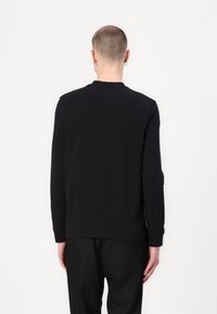 Maglietta nera a maniche lunghe con scollatura a girocollo e polsini a coste, caratterizzata da una texture liscia e dettagli di cucitura discreti sulla parte posteriore.