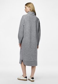 Γκρίζα πλεκτή φόρεμα με ψηλό γιακά και μακριά μανίκια, με πλάγιο σκίσιμο και ριμπ τελείωμα. Συνδυάζεται με λευκά αθλητικά παπούτσια.