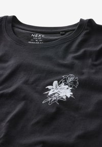 Schwarzes Baumwoll-T-Shirt mit einem weißen Blumenmuster auf der unteren Vorderseite, regulärer Schnitt, mit Rundhalsausschnitt und kurzen Ärmeln.