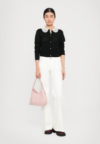 Woman wearing black buttoned sweater with white lace collar, white wide-leg pants, burgundy shoes, and holding a pink handbag.
