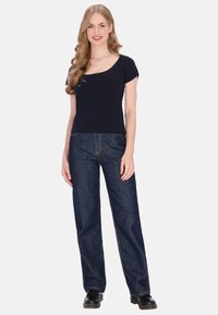 Tengerészkék bordázott rövid ujjú póló laza szabású sötét farmernadrággal párosítva. A modell fekete cipőt visel, és egy egyszínű háttér előtt áll.