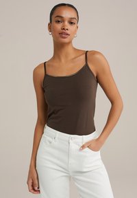 Barna, testhez simuló camisole vékony pántokkal, kerek nyakkivágással, magas derekú fehér farmernadrággal párosítva. Sima anyagú kivitel.