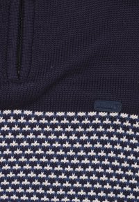 Marineblauwe gebreide half-zip trui met een gestructureerd blokpatroon in wit en lichtblauw, voorzien van een rubberen J&Joy logo-label aan de linkerkant.