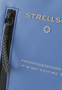Blauwe textuuroppervlakte met grijs "STRELLSON" logo, weersbestendige rits en een koordtrekker. Heeft locatiecoördinaten en een hashtag-detail.