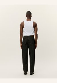 Vista trasera de una persona que lleva una camiseta sin mangas blanca y unos vaqueros negros de tiro alto. Los vaqueros tienen dos bolsillos traseros y un diseño de pierna recta.