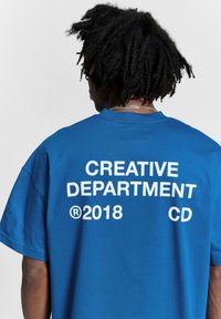 Blue cotton t-shirt with a loose fit. Back features large white text: "CREATIVE DEPARTMENT," "(R)2018," and "CD." Short sleeves, crew neckline.