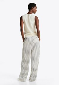 Bezrękawnik dzianinowy w kolorze kremowym z teksturowanym wzorem, w połączeniu z szerokimi spodniami w paski z pionowymi liniami i okrągłymi akcentami.