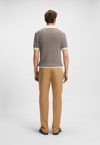 Polo a maniche corte in maglia strutturata nei colori nero e bianco con dettagli color crema. Abbinata a pantaloni beige e scarpe nere, vista da dietro.