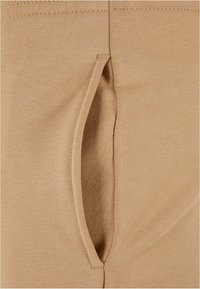 Beige Stretchstoff mit seitlichem Schlitzdetail, glatter Textur und sauberen Nähten. Der Stoff wirkt leicht und formschmeichelnd.