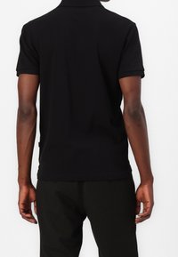 Polo noir en coton, avec un col classique, des manches courtes et une coupe ajustée, associé à un pantalon à rayures.