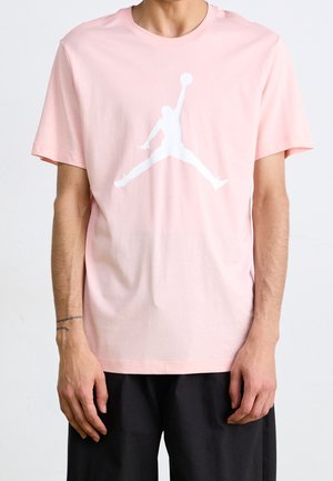 Jasnoróżowa bawełniana koszulka z okrągłym dekoltem i krótkimi rękawami. Na przodzie znajduje się duże białe logo Jumpman.