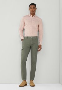 Chemise à manches longues avec des rayures verticales rouges et blanches, associée à un pantalon cargo fuselé couleur olive et des chaussures en cuir beige à lacets.