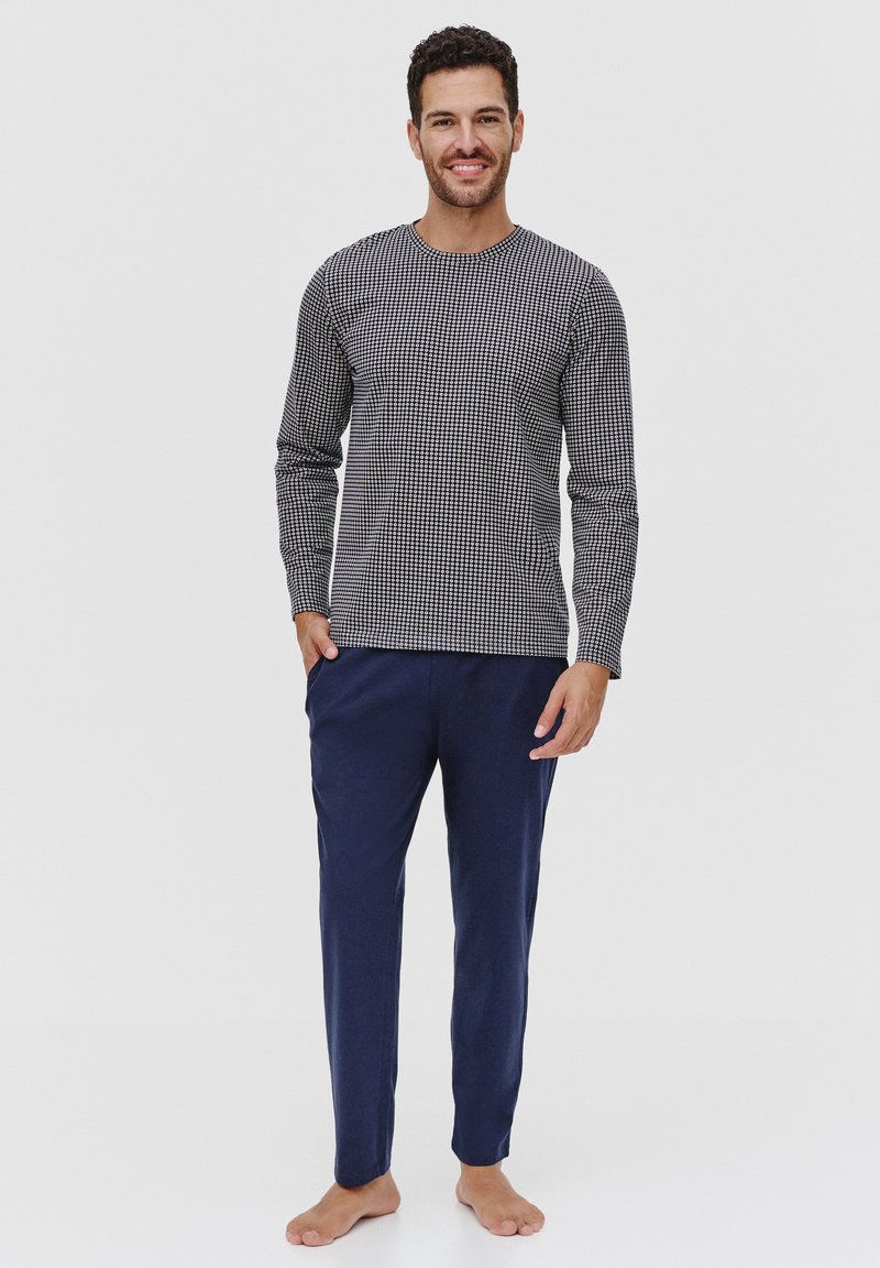 Męski zestaw piżamowy składający się z wzorzystej, czarno-białej bluzki z długim rękawem oraz jednolitych granatowych spodni. Wygodne dopasowanie, miękki materiał.