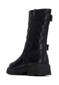 Botas negras de cuero acolchado hasta la rodilla, con cremallera lateral, correa ajustable y suela gruesa y texturizada.