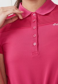 Polotröja i klargul, med ribbad krage, knappslå med rosa knappar och texturerade horisontella ränder över bröstet.