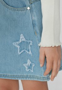 Jupe en denim délavé avec deux écussons en forme d'étoile brodés. Ourlet fini et poche latérale, associée à un haut à manches longues en côte.