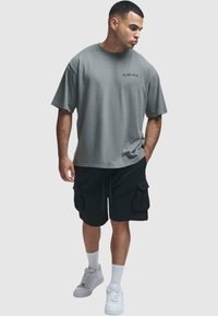Grå oversized t-skjorte med sidesømmer, kombinert med svarte cargo-shorts med flere lommer. Båret med hvite joggesko og sokker.