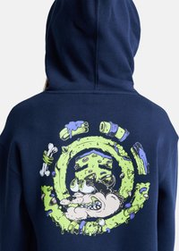 Le hoodie bleu marine présente un graphique coloré au dos d'un visage cartoonish entouré d'un cercle vert gluant et d'accents en forme d'os.