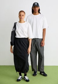Hvite oversized t-skjorter, svart joggeskirt med lommer, grå vide bukser, svarte sneakers og svart caps med logoakenter.