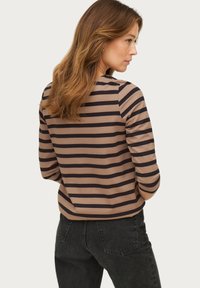 Gestreiftes Langarmoberteil in Braun und Marineblau mit einem abgerundeten Ausschnitt. Weicher Stoff, figurbetontes Design und aufgerollte Ärmelbündchen. Schwarze hochtaillierte Jeans.