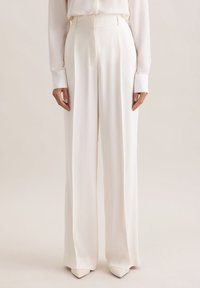 Wijduitlopende broek van witte stof met een gladde textuur, met een hoge taille en naadloos voorpand, gecombineerd met puntige hakken.