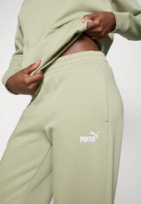 Pantaloni sportivi verde oliva realizzati in tessuto morbido, dotati di una vita elasticizzata e tasche laterali. Logo Puma ricamato di colore bianco sulla coscia.