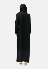 Zwarte abaya gemaakt van gladde stof met lange mouwen en een ontwerp tot op de grond, aangevuld met een bijpassende hijab en subtiele metalen accenten.