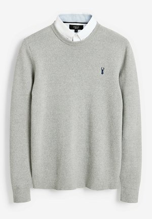 Hellgrauer Strickpullover mit Rundhalsausschnitt, gerippter Textur und einem kleinen marineblauen Logo auf der Brust. Darunter ist ein weißes Hemd mit Kragen zu sehen.