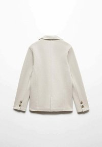 Beige kavaj med en texturerad yta, enfärgad design, snedskuren krage och två knappdetaljer på varje manschett.