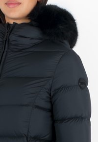 Černá péřová bunda s vysokým límcem, zdobená hřejivým černým kožíškem. Materiál je hladký a lesklý, s vodorovně prošívanými sekcemi.