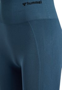 Close-up van blauwe naadloze sportleggings met getextureerde chevronpatronen en het "hummel" merklogo op de tailleband.