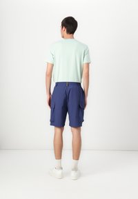 Light green short-sleeve shirt, navy cargo shorts with side pockets, and white sneakers. Simple design, soft texture, elastic waistband.