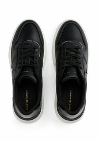 Sneakers neri a bassa punta con suole bianche, design con lacci e suole marchiate, visti dall'alto su uno sfondo bianco.