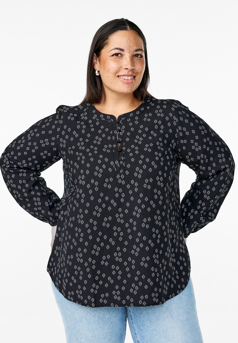 Blusa nera a fantasia con scollatura rotonda, maniche lunghe, chiusura a bottone e una texture morbida con disegni geometrici bianchi.
