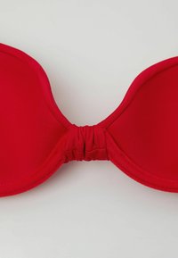 Rotes, gepolstertes Bikinioberteil mit gerafftem Stoffdetail in der Mitte, flach auf einem hellen Hintergrund liegend.