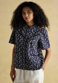 Lühikeste varrukatega tumesinine pluus valgete lillemustritega, ümmarguse krae, kahe esipocket'i ja tekstuuriga kangaga.