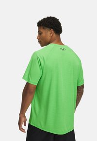 Camiseta deportiva verde neón de manga corta, con cuello redondo y una textura sutil. Presenta un logo en la parte superior de la espalda.
