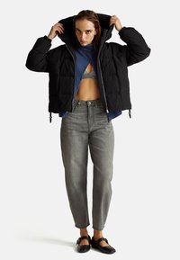 Czarna kurtka typu puff z kapturem, pikowana, z elastycznymi mankietami, noszona na niebieskiej bluzie. W zestawie z szarymi dżinsami z wysokim stanem i płaskimi butami.